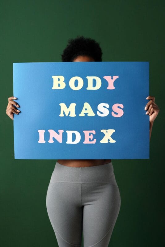 African American woman holding a colorful BMI sign, promoting health and wellness.