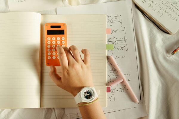 A student calculates math equations using an orange calculator and notebook for study.