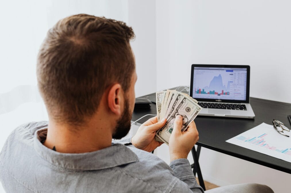 a man sitting with money and laptop